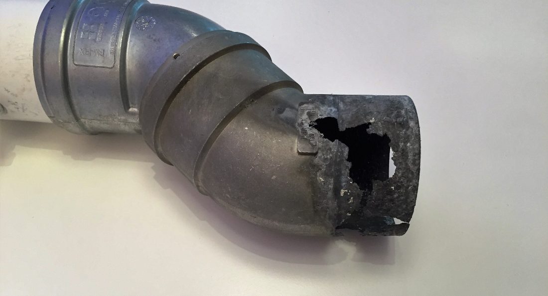 Een aluminium bocht van een rookgasafvoer met een gat, doorgevreten door zuur condenswater