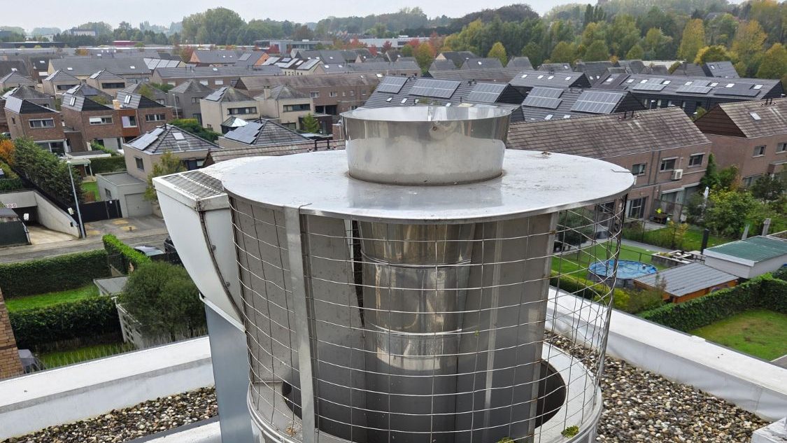 Oude CLV-kap op het platte dak van een appartementsgebouw: inox trommel met een band gaas en de rookgasbuis in het midden van het deksel